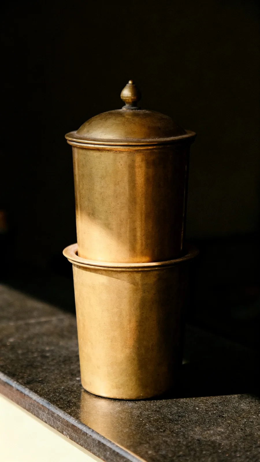 A traditional South Indian brass coffee filter, its domed upper chamber seated in the vessel below