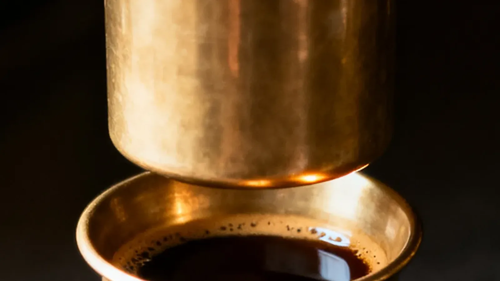 A brass filter chamber above a cup, close up on a dark ground