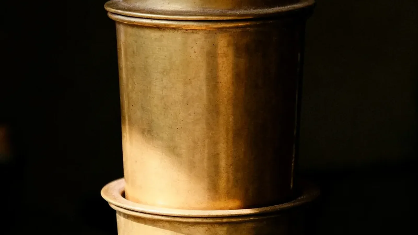 A brass South Indian coffee filter on a dark ledge