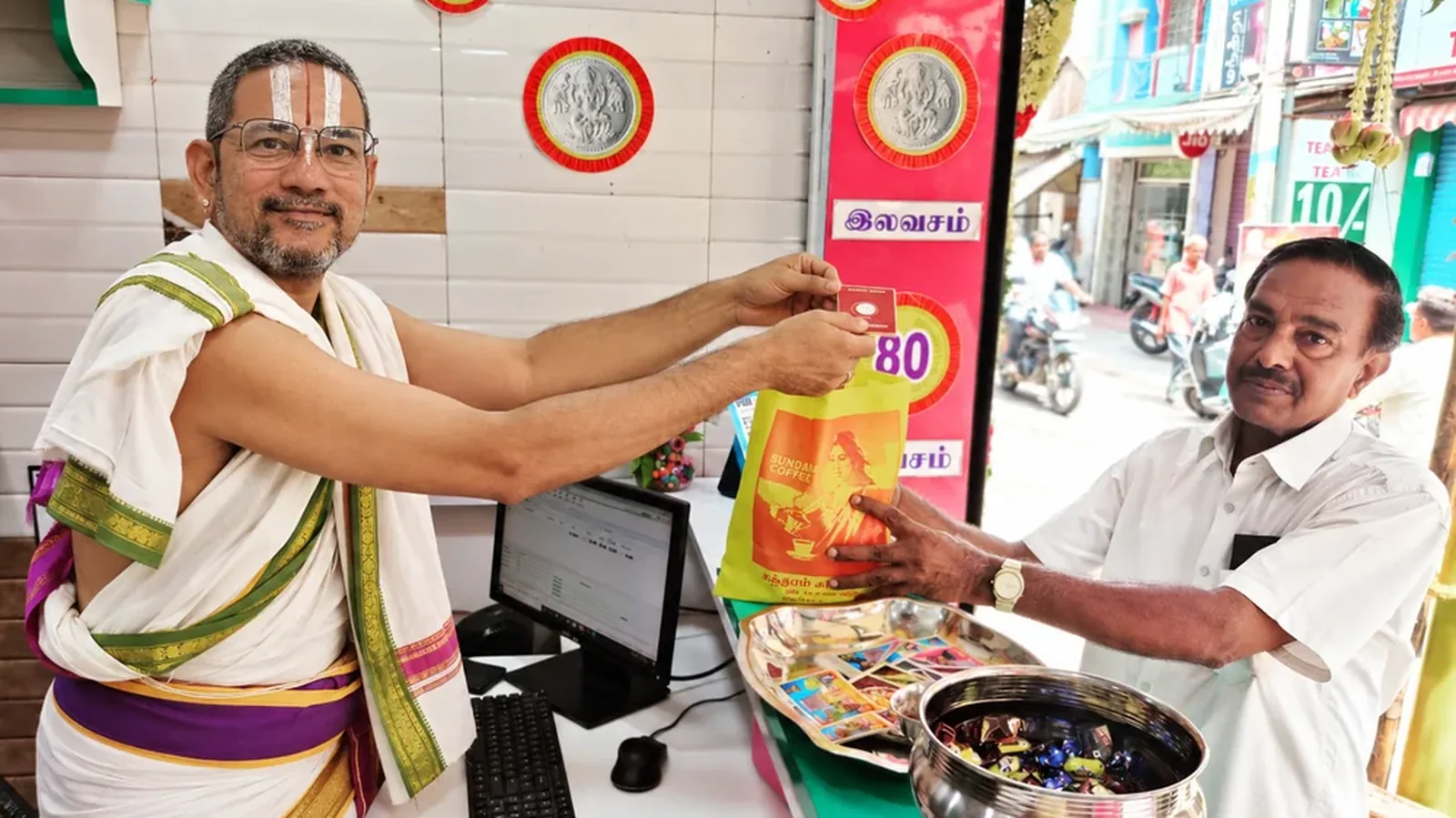 Rajagopalan N. behind the counter of Sundaram Coffee Works, handing a packet across