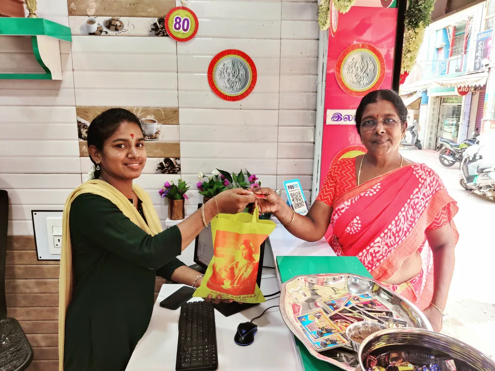 Inside the shop: a customer takes a printed cloth bag of coffee across the counter, with Kasukadai Street visible through the open front